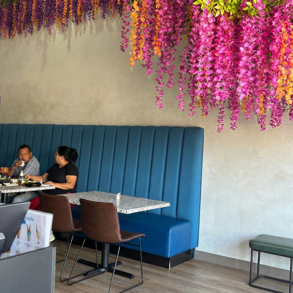 Restaurant interior with a blue booth, two diners, patterned partition, floral ceiling decor, tables, and a bench.