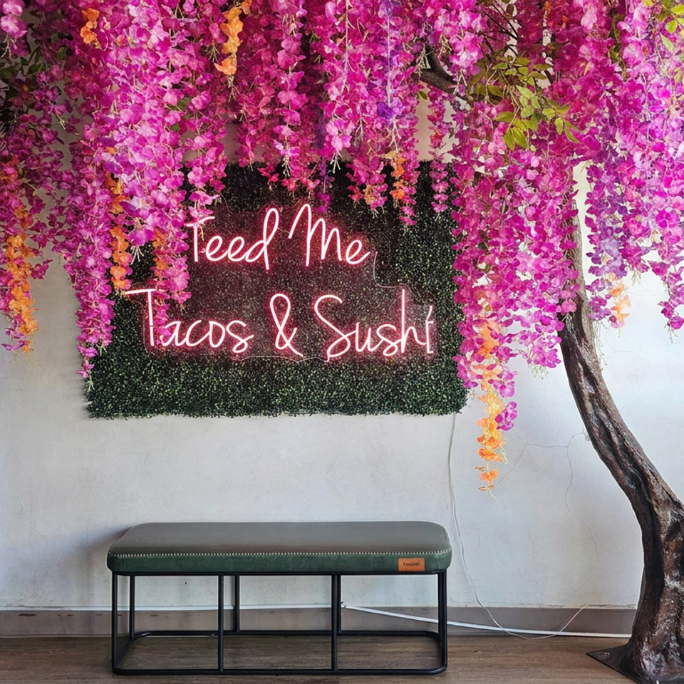 Restaurant photo spot with cascading pink and orange flowers, a bench, and neon sign reading “Feed Me Tacos & Sushi.”